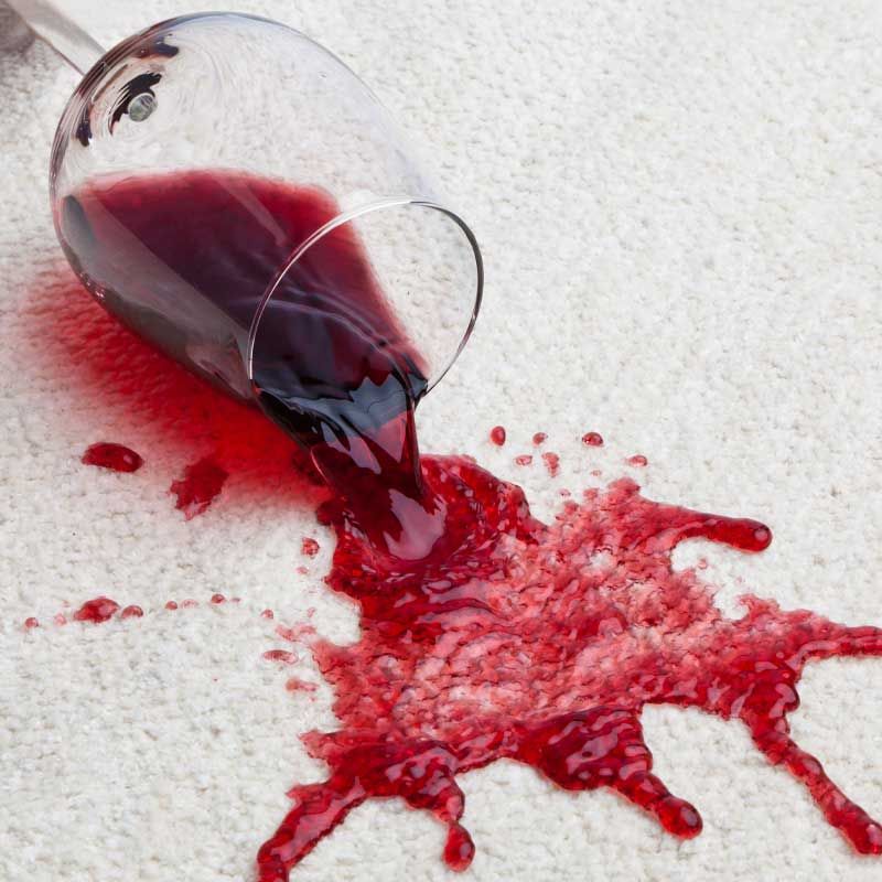 A glass of wine spilling on a white carpet